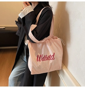 Detail of pink drawstring tote bag showing crinkled nylon fabric and red logo lettering