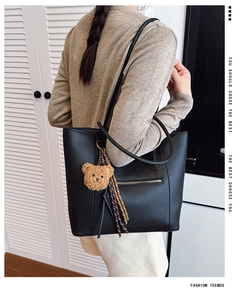 Detail of black pebbled leather tote bag featuring a front zipper pocket and plush bear charm