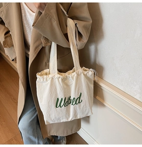 Detail of white canvas drawstring tote bag with green script lettering worn by model