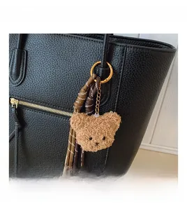 Detail view of plush brown bear bag charm with woven rope and golden metal ring