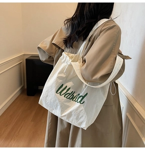 Detail of white nylon tote bag with green script lettering and drawstring closure