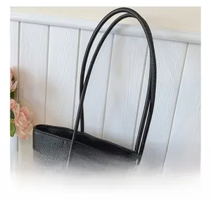 Detail of black pebbled leather tote bag with sturdy handles and gold metal ring accents