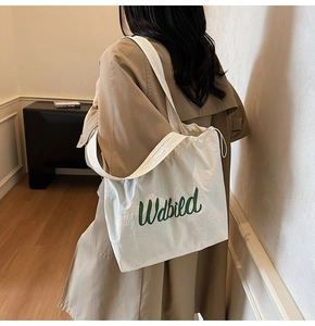 Detailed view of white drawstring tote bag with green Udbild logo worn with a beige coat