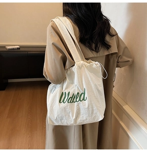 Close-up of white canvas tote bag with green Wasted text and drawstring closure
