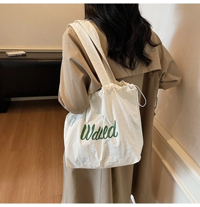 Detail of white canvas drawstring tote bag with green Walked script text and shoulder strap