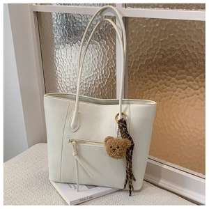 Detail shot of off-white lychee texture tote bag with front zip pocket and bear charm