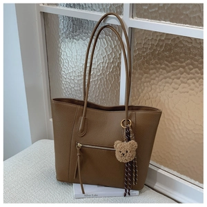 Detailed texture of brown litchi grain leather tote bag with cute plush bear keychain