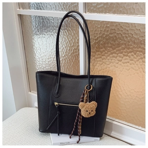 Detail of black pebbled leather tote bag with metal zipper and cute bear charm