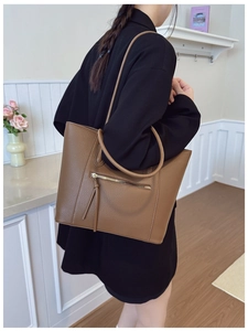 Brown lychee leather tote bag with tassel zipper detail shown on a model in a modern room