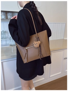 Brown lychee leather tote bag shown with plush bear charm on a model in lifestyle setting