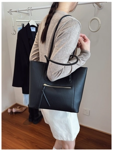 Detail of a large black pebble leather tote bag with exterior zip and tassel on a model