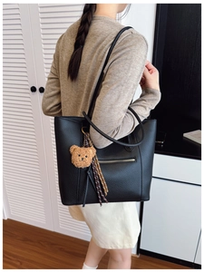 Detail of black pebbled leather tote bag with metallic zipper and cute bear charm pendant