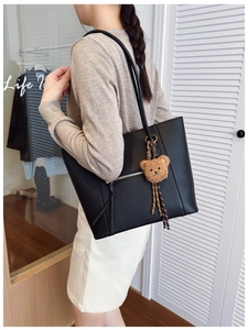 Detail of black pebbled leather tote bag with front zipper and bear charm worn by model