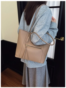 Detail of tan pebble leather tote bag showing a front zipper pocket and long shoulder straps