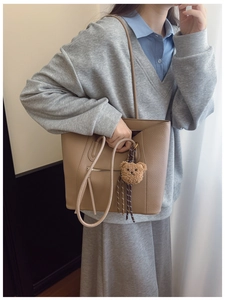 Macro detail of khaki litchi grain leather tote bag with stylish plush bear pendant accessory