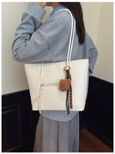 Detail of white lychee leather tote bag with zip pocket and brown plush bear charm