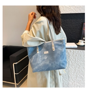 Dettaglio della borsa tote in denim blu con etichetta in pelle e manici sottili sopra un trench