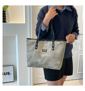 Dettaglio della borsa tote grigia marmorizzata con lunghi manici in pelle nera e logo moda