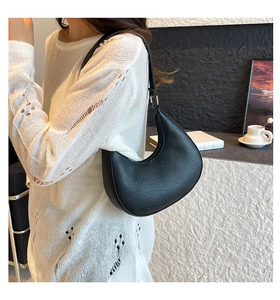 Detailed view of black litchi pattern crescent bag worn as an elegant underarm bag