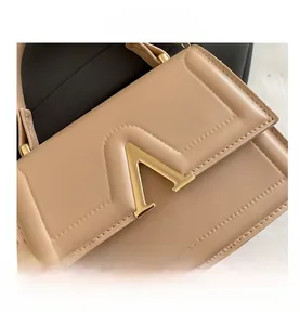 Close-up of beige leather handbag featuring a prominent gold V-shaped metal buckle and stitching