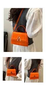 Detail of orange handbag with gold V-buckle closure and adjustable shoulder strap