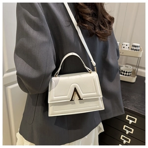 Detail of white leather crossbody bag with gold A-shaped buckle on a model in gray blazer