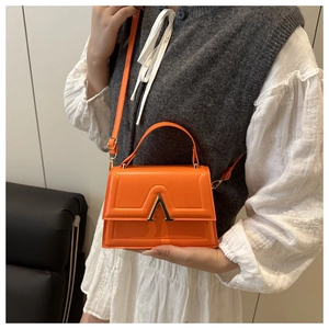 Close-up of bright orange leather handbag with gold V-shape clasp and top handle