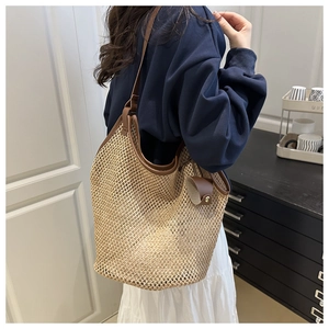Close-up of woven straw tote bag with brown leather trim and hanging leather accessory