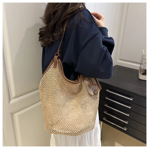 Detail of hand-woven straw tote bag featuring brown leather straps and reinforced edges