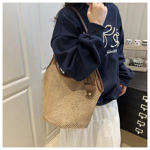 Detail of straw tote bag with brown leather handles and strap on a model shoulder