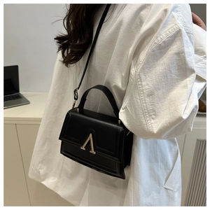 Detail of minimalist black matte leather crossbody bag with gold V-shape metal clasp