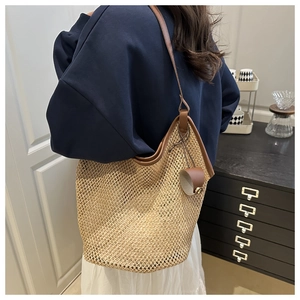 Detail of straw tote bag with brown leather strap and trim against a minimalist backdrop