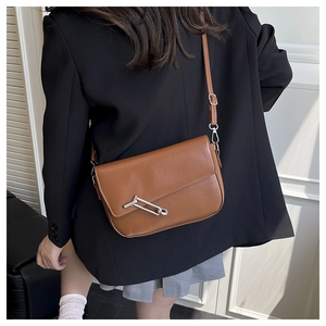 Detail view of a vintage brown leather saddle bag with silver pin buckle and slim strap