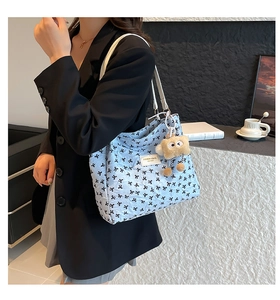 Detail view of light blue quilted tote bag with black bow patterns and a plush charm
