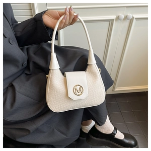 Detail of cream woven shoulder bag with golden M logo clasp held by a model