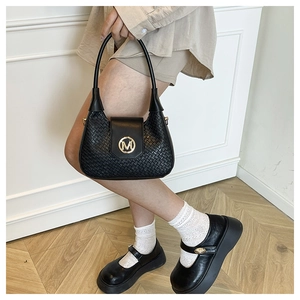 Primer plano de bolso bandolera tejido negro con hebilla M dorada en una modelo
