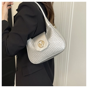 Silver woven shoulder bag detail featuring gold metal M logo on model with black suit
