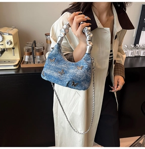 Détail du sac en jean bleu avec poignée argentée, décor papillon et chaîne métallique