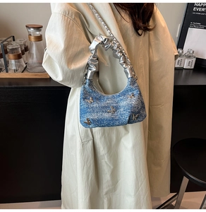 Détail du sac plissé en denim bleu avec breloques papillon et chaîne argentée