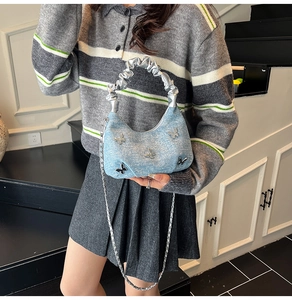Détail du sac croissant en denim bleu clair avec papillons argentés et bandoulière