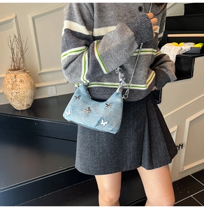 Détail du sac croissant en denim bleu clair avec papillons argentés et bandoulière chaîne