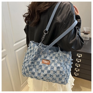 Close-up of blue and white checkered denim tote bag featuring frayed edges and leather patch