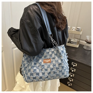 Detail of denim checkerboard shoulder bag with frayed edges and leather chain strap