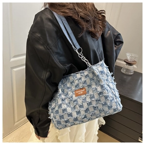 Detail of blue and white checkered denim tote bag with frayed edges and leather chain strap