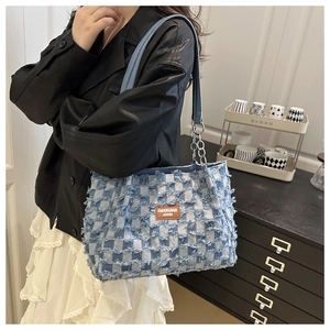 Detailed shot of checkered denim tote bag featuring frayed edges and brown leather tag