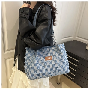 Close-up of denim checkerboard tote bag featuring frayed edges and a brown leather tag