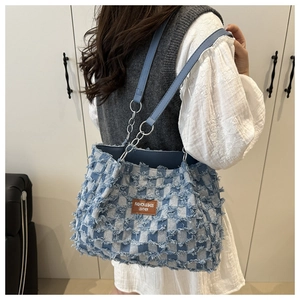 Detail of blue denim tote bag with frayed edges and silver metal chain strap for women