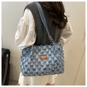 Detail of blue plaid tote with frayed edges, leather tag and silver chain strap
