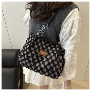 Detail of tweed checkered tote bag with fringe edges and silver chain strap on model