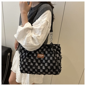 Detail of checkered denim tote bag featuring raw frayed edges and leather brand label